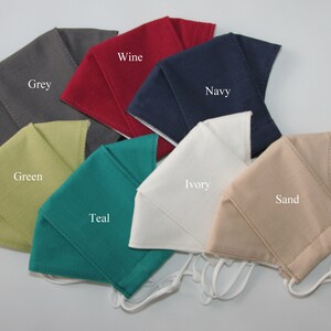 May include: A set of ten fabric face masks in various colors, including grey, green, teal, ivory, sand, wine, and navy. Each mask has a simple design and is made of a soft, breathable fabric.