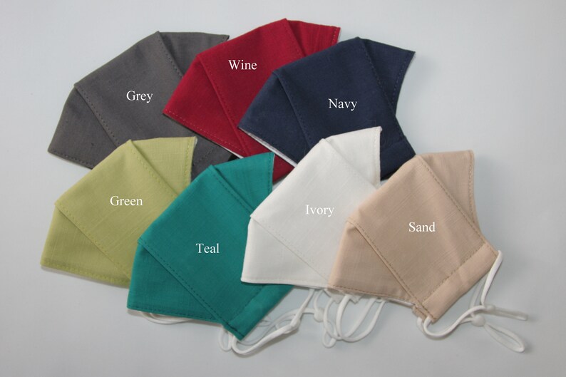 May include: A set of ten fabric face masks in various colors, including grey, green, teal, ivory, sand, wine, and navy. Each mask has a simple design and is made of a soft, breathable fabric.