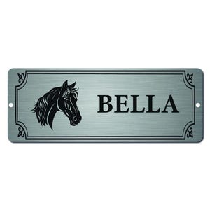 Puede incluir: Un letrero metálico rectangular con acabado plateado cepillado. El letrero presenta una silueta de cabeza de caballo negra a la izquierda y el nombre "BELLA" en letras negras en negrita a la derecha. Bordes y adornos de esquina negros decorativos completan el diseño.