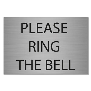 May include: A rectangular sign made of brushed metal, featuring the black text "PLEASE RING THE BELL". The text is centrally aligned. The sign's design is simple and modern, suitable for a door or entrance.