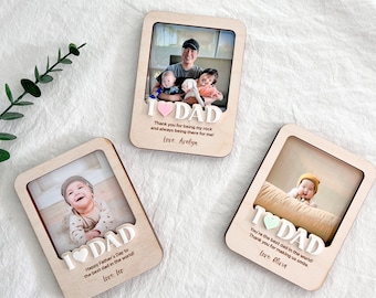 May include: Three wooden photo frames with a heart and the word "I love Dad" on each. The frames have photos of children and a father. The text on the frames reads "Thank you for being my rock and always being there for me! Love, Avelyn", "Happy Father's Day to the best dad in the world! Love, Leo", and "You're the best dad in the world! Thank you for making us smile. Love, Olivia".