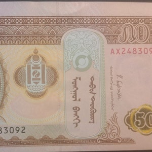 May include: A 50 Mongolian Tugrik banknote featuring a portrait of Genghis Khan, the founder of the Mongol Empire, in the center. The banknote is printed in shades of brown, yellow, and green. The text "AX2483092" is printed on the banknote.