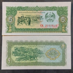 Pode incluir: Uma nota de banco laosiana de 5 Kip com um design verde e amarelo. O anverso da nota representa uma cena de pessoas trabalhando em uma loja. O verso da nota mostra elefantes transportando toras em uma floresta. O texto "ສາທາລະນະລັດປະຊາທິປະໄຕປະຊາຊົນລາວ" e "ທະນາຄານເເຫ່ງຊາດ" está impresso na nota.