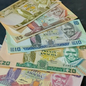 May include: A stack of five Zambian kwacha banknotes, featuring different denominations: 2, 5, 10, 20, and 50 kwacha. Each banknote features a portrait of a different person and a unique design.
