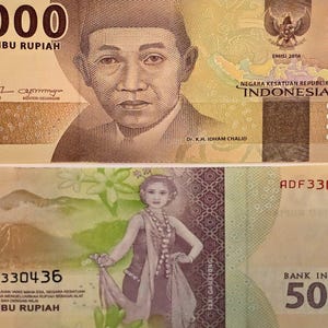 Könnte beinhalten: Nahaufnahme von zwei indonesischen 5.000 Rupiah-Banknoten. Die obere Banknote zeigt ein Porträt eines Mannes und den Text "LIMA RIBU RUPIAH". Die untere Banknote zeigt eine Frau in traditioneller Kleidung und den Text "BANK INDONESIA 5000".