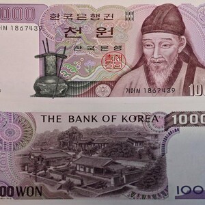 May include: A Korean 1000 Won banknote. The front features a portrait of a man in traditional attire, with Korean text and the number 1000. The back shows a detailed illustration of a traditional Korean building and the text "THE BANK OF KOREA".