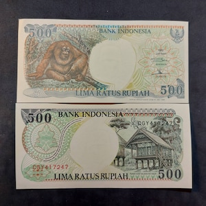 May include: A 500 Rupiah Indonesian banknote featuring an orangutan on the front and a traditional house on the back. The text "LIMA RATUS RUPIAH" is printed on both sides.