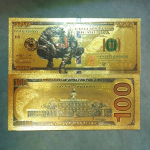 May include: Two gold-colored paper bills with the text "100" printed on them. The top bill features a black and gold image of a creature with a large head and claws. The bottom bill features a gold image of a building with a dome.