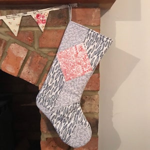 May include: A white and blue patchwork Christmas stocking with a red and white floral pattern on one side. The stocking is hanging on a brick fireplace mantel.