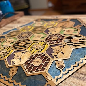 May include: Wooden board game with hexagonal tiles, featuring various resource symbols and numbers. The board has a blue and brown border, with a natural wood finish on the tiles. A unique, handcrafted board game.