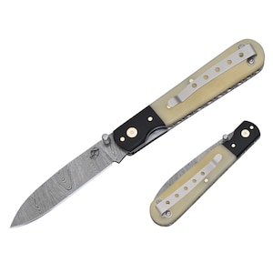 May include: A folding pocket knife with a white bone handle and a Damascus steel blade. The knife has a black bolster and a brass pin.