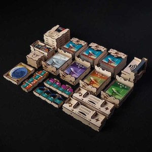 May include: Wooden board game organizer with various compartments and boxes. The boxes contain game cards with colorful illustrations of planets, satellites, and space themes. Some boxes have the word "SET" and "LASEROH" printed on them.