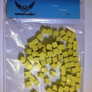 May include: A clear plastic bag containing numerous yellow 8 mm wooden cubes. The bag has a blue label that reads "8 MM Wooden Cubes" and "Mayday Games". The label also states "100% Wood" and includes a logo.