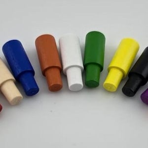 May include: A collection of eleven wooden pegs in various colors, including yellow, red, cream, blue, brown, white, green, black, purple, and pink. The pegs are arranged in a curved line against a white background.