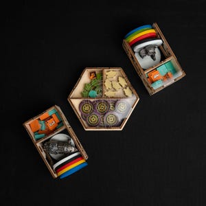 May include: Wooden game organizer with various game pieces. The organizer includes a hexagonal box with clear lid, and three rectangular boxes. The game pieces include colorful tokens, gears, and car-shaped pieces. The colors include orange, yellow, green, and purple.