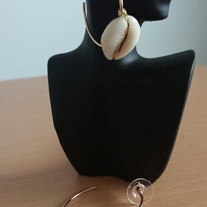 May include: A pair of gold hoop earrings with a white cowrie shell attached to each hoop.
