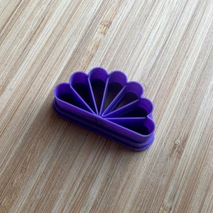 Puede incluir: Cortador de galletas de pl&aacute;stico morado en forma de abanico con siete secciones.