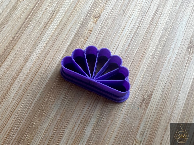 Puede incluir: Cortador de galletas de pl&aacute;stico morado en forma de abanico con siete secciones.