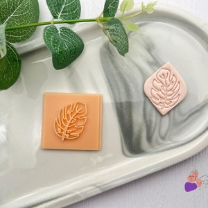 Puede incluir: Dos sellos de goma rosa con un diseño de hoja. Los sellos están sobre una superficie de mármol blanco.