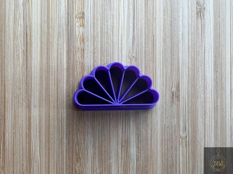 Puede incluir: Cortador de galletas de pl&aacute;stico morado en forma de abanico con siete secciones.