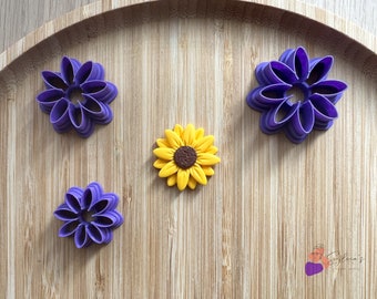 Könnte beinhalten: Drei violette blütenförmige Ausstecher und eine gelbe Fondant-Sonnenblume auf einer Holzoberfläche.