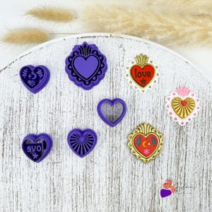 Peut inclure: Une collection d'emporte-pièces en forme de cœur de différentes formes et couleurs. Les emporte-pièces comprennent des cœurs violets, dorés et rouges avec des motifs décoratifs, dont le mot "love" sur l'un d'eux.