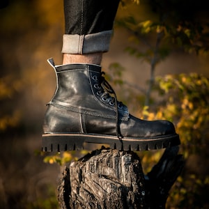 May include: A black leather boot with laces and a thick sole, resting on a weathered tree stump.