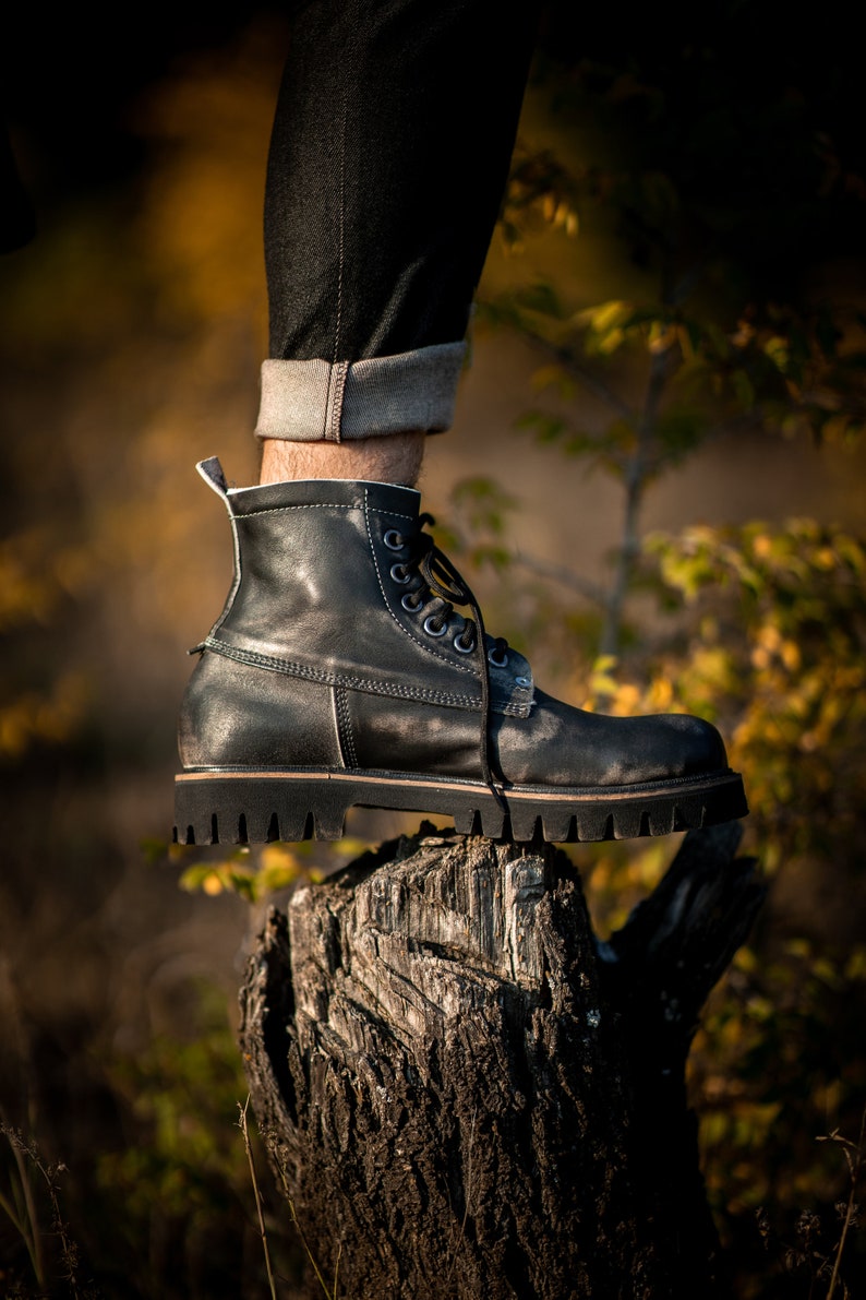 May include: A black leather boot with laces and a thick sole, resting on a weathered tree stump.