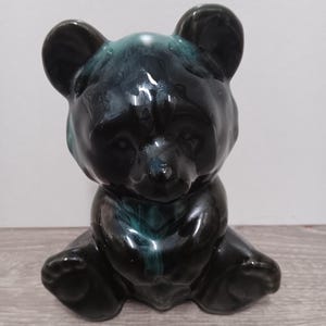 May include: A ceramic bear figurine in a sitting position. The bear is primarily black with streaks of teal and a glossy finish. The figurine has rounded ears, a small nose, and its paws are visible.