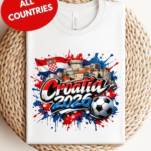 A white t-shirt with a graphic design featuring the text "Croatia 2026" and a soccer ball, surrounded by splashes of red, blue, and white colors.