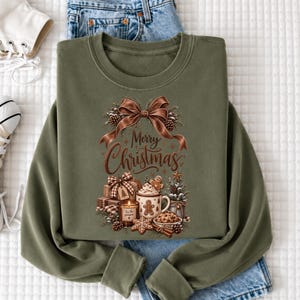 A green sweatshirt with a Christmas-themed design, including a bow, pine cones, a mug, and other holiday-related items, along with the text "Merry Christmas".