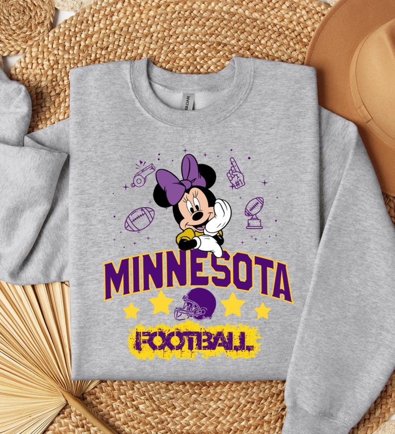 May include: A gray sweatshirt featuring Minnie Mouse with a purple bow, holding a football. The text "MINNESOTA FOOTBALL" is in purple and yellow. Football-themed graphics surround the character.