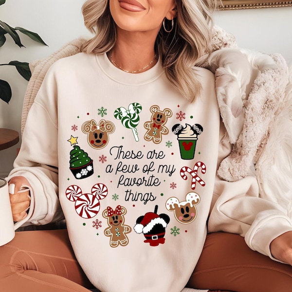 Könnte beinhalten: Ein cremefarbenes Sweatshirt mit Rundhalsausschnitt und einem zentralen Aufdruck mit dem Text "These are a few of my favorite things", umgeben von weihnachtlichen Symbolen wie Lebkuchenfiguren, Zuckerstangen, Pfefferminzspiralen und Leckereien.