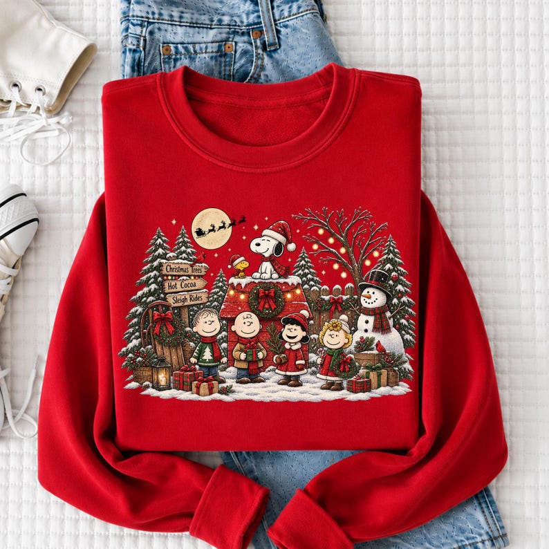A red sweater with a Christmas-themed design featuring characters from the Peanuts comic strip, including Snoopy, Charlie Brown, and Woodstock, along with a snowy winter scene.