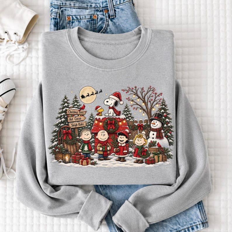 A gray sweatshirt with a Christmas-themed design featuring characters from the Peanuts comic strip, including Snoopy, Woodstock, and other beloved Peanuts characters, along with a snowy winter scene.
