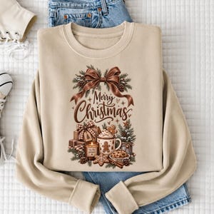 A beige sweatshirt with a Christmas-themed design, including a bow, pine cones, gingerbread cookies, and a mug with a "Merry Christmas" message.