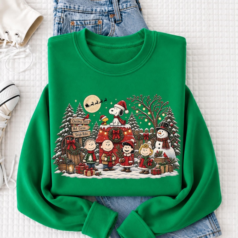 A green sweatshirt with a Christmas-themed design featuring characters from the Peanuts comic strip, including Snoopy, Charlie Brown, and Woodstock, along with a wreath and presents.