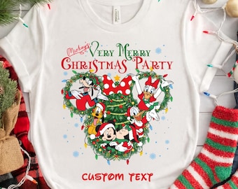 May include: A white t-shirt featuring a graphic of Disney characters including Mickey Mouse, Minnie Mouse, Goofy, Pluto, Donald Duck, and Daisy Duck arranged within a Christmas tree shape, with the text Mickey's Very Merry Christmas Party.