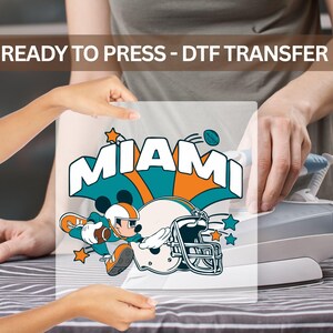 The image is a collage of two people interacting with a Miami Dolphins football helmet, with one person holding the helmet up to the other person's face.