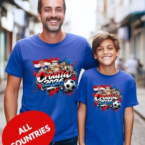 A man and a young boy are standing together, both wearing blue t-shirts with a graphic design featuring the text "Cromatia 2020" and a soccer ball.