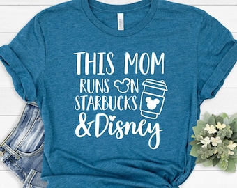 May include: A teal blue short-sleeve t-shirt with white text that reads THIS MOM RUNS ON STARBUCKS & Disney, featuring a small Mickey Mouse head icon and a graphic of a coffee cup with a Mickey Mouse head icon on the side of the cup.