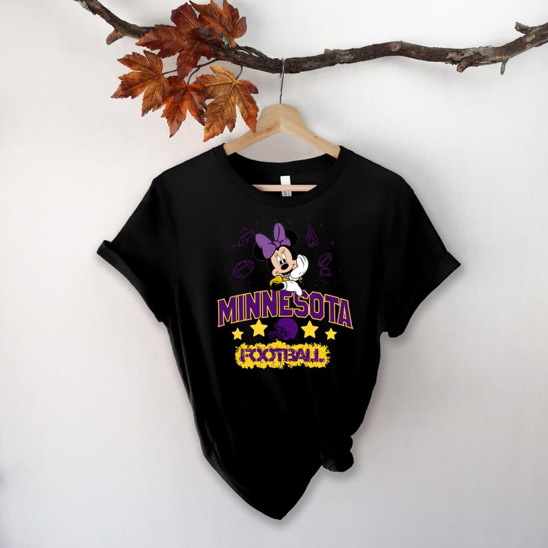 May include: Black t-shirt featuring a graphic of Minnie Mouse in a purple bow and outfit, with the text "MINNESOTA FOOTBALL" in purple and yellow. The design includes stars and football-themed illustrations.