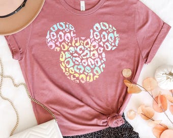 May include: A mauve short-sleeved t-shirt featuring a central graphic of a mouse head silhouette filled with a multicolored pastel leopard print pattern. The shirt has a crew neckline and a standard fit, displaying a clear brand label at the neck.
