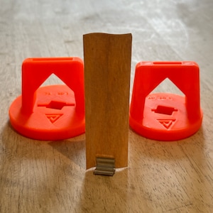 May include: Three orange plastic tile spacers with the text "74 303" and a triangle symbol on each. A brown cardboard piece is in the center.