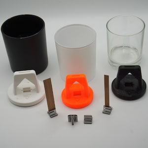 May include: Three glass candle jars in black, white, and clear glass with lids in black, white, and orange. Each lid has a small metal handle. Three wooden wicks are included.
