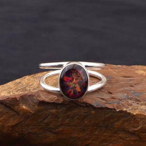 May include: A silver ring with an oval-shaped, multi-colored opal gemstone. The opal displays a vibrant array of colors, including red, orange, yellow, and green. The ring has a split shank design.