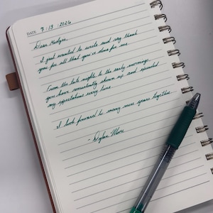 May include: A spiral-bound notebook with lined white paper featuring a handwritten note in dark green ink dated 7/13/2026. The note reads: Dear Kedyie, I just wanted to write and say thank you for all that you've done for me. A green pen rests on the page.