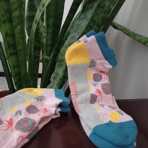 May include: Two pairs of colourful socks with a floral pattern. The socks are pink, grey, yellow and teal.