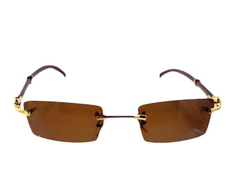 May include: Rimless sunglasses with brown tinted lenses and gold-colored accents. The rectangular lenses are connected by a thin gold bridge. The temples are a dark brown color.