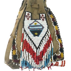 Puede incluir: Una bolsa de cuero marrón con un diseño de cuentas. La bolsa tiene un cierre de cordón y una franja de cuentas. Las cuentas son blancas, rojas, azules y negras.